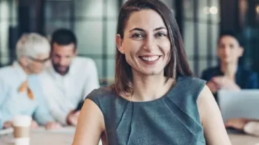 Smiling woman in a gray dress in an office meeting.